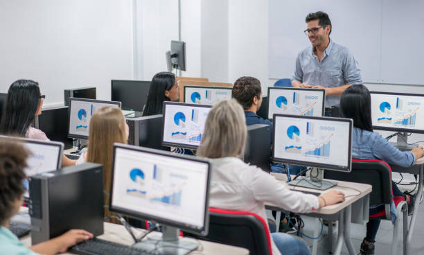 Happy teacher giving an IT class at school to a group of students using computers - education concepts. Image on screens were made from scratch by us.
